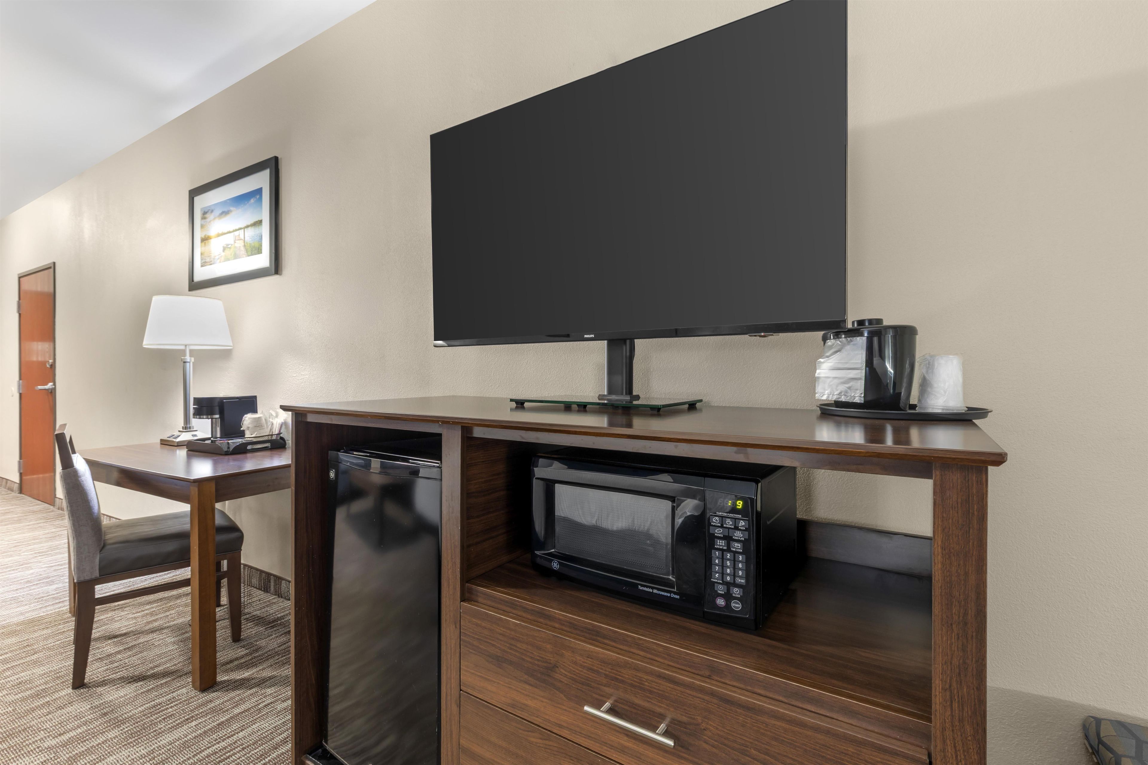 Una habitación de hotel con un escritorio de madera, un microondas, una cafetera y un televisor.