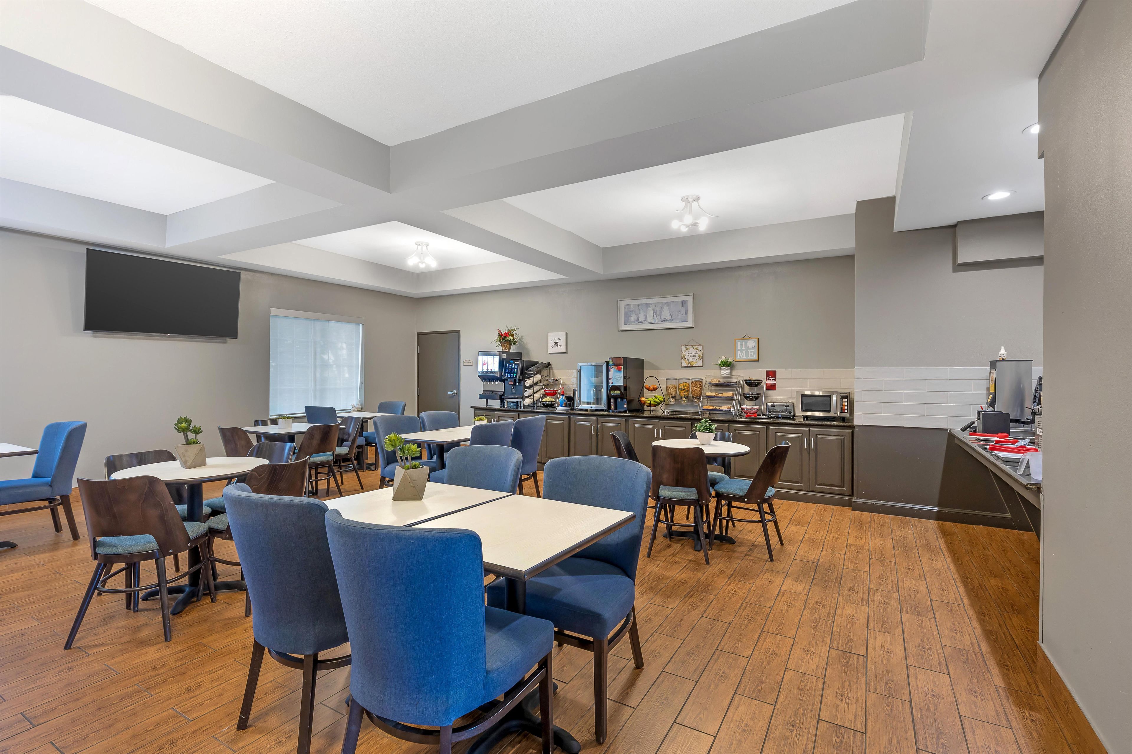 A dining area with tables and chairs, a kitchen area with appliances, and a flat-screen TV mounted on the wall.