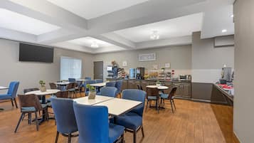 A dining area with tables and chairs, a kitchen area with appliances, and a flat-screen TV mounted on the wall.