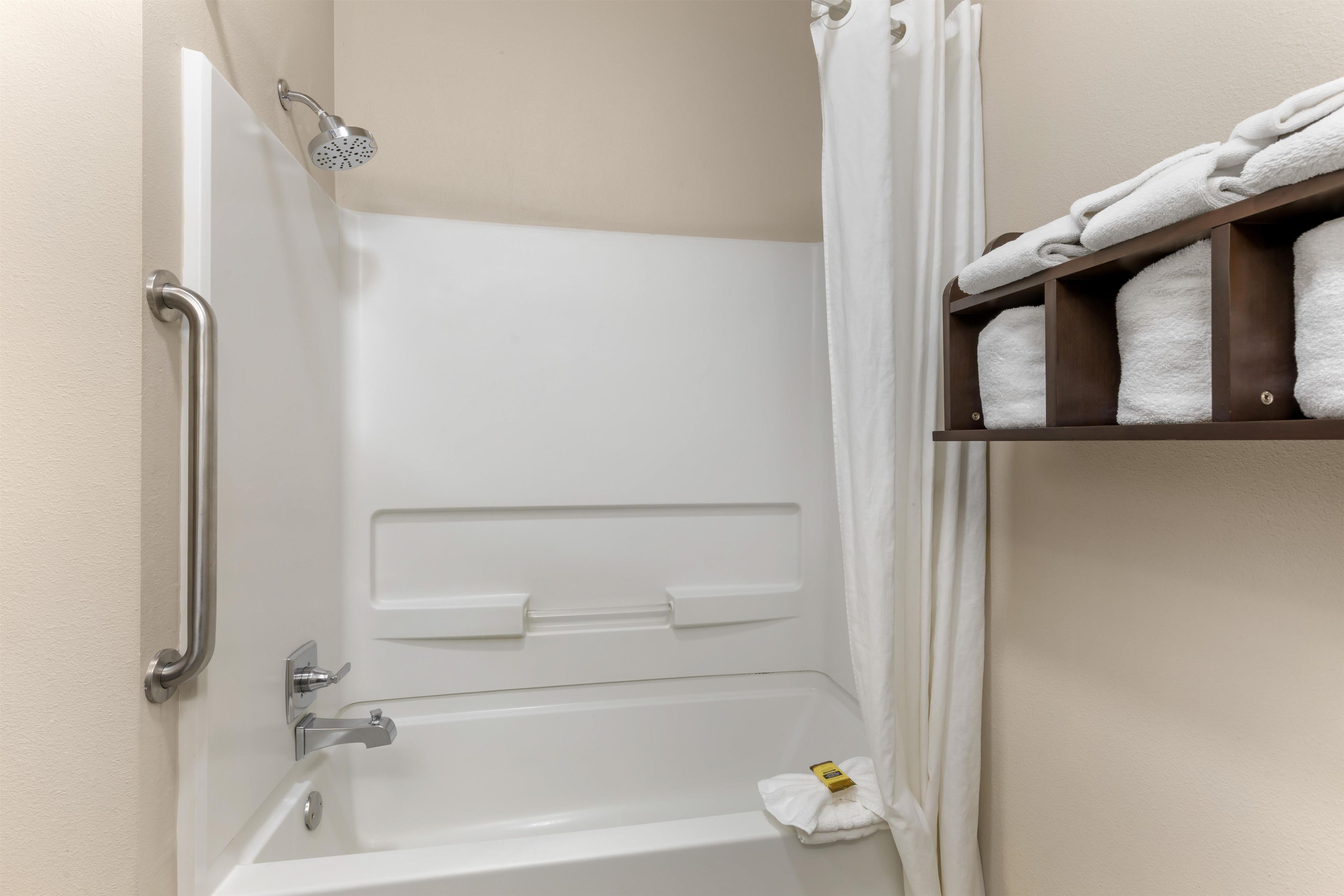 Un baño con bañera, ducha, toallero y repisa con toallas dobladas.