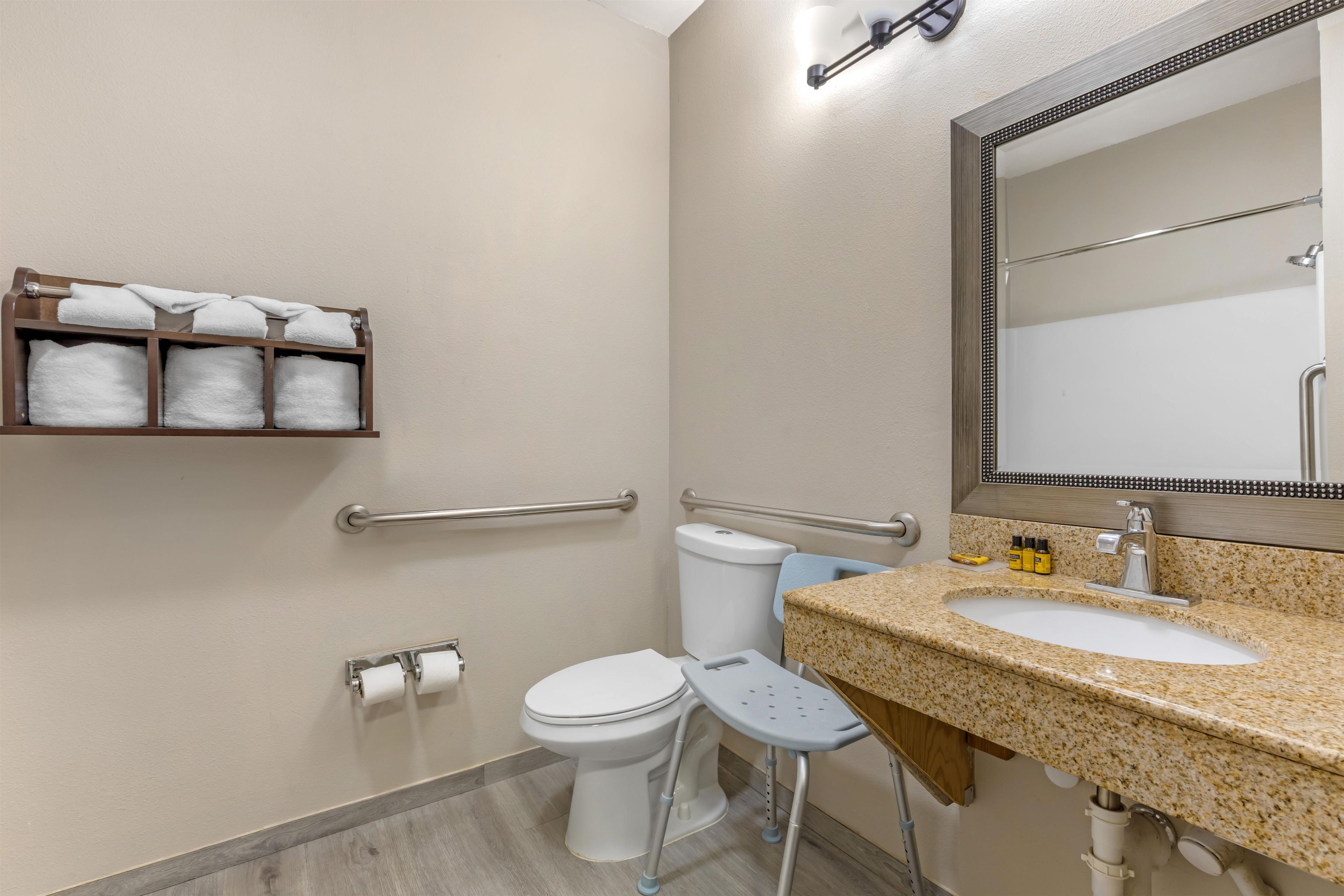 Un baño con inodoro, lavamanos, espejo, toallero y barra de apoyo.