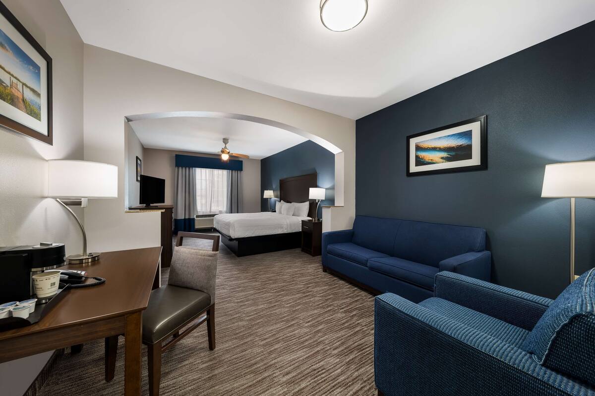 Una habitación de hotel con una cama, un sofá azul, un escritorio con una lámpara y una silla.