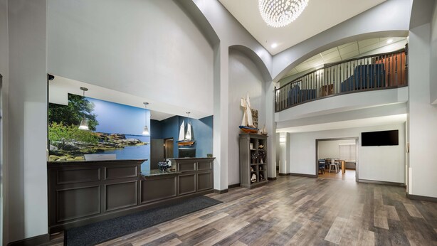 A spacious lobby with a reception desk, a large mural, and a staircase leading to a balcony. - Best Western Plus Lake Dallas Inn & Suites (Lake Dallas)