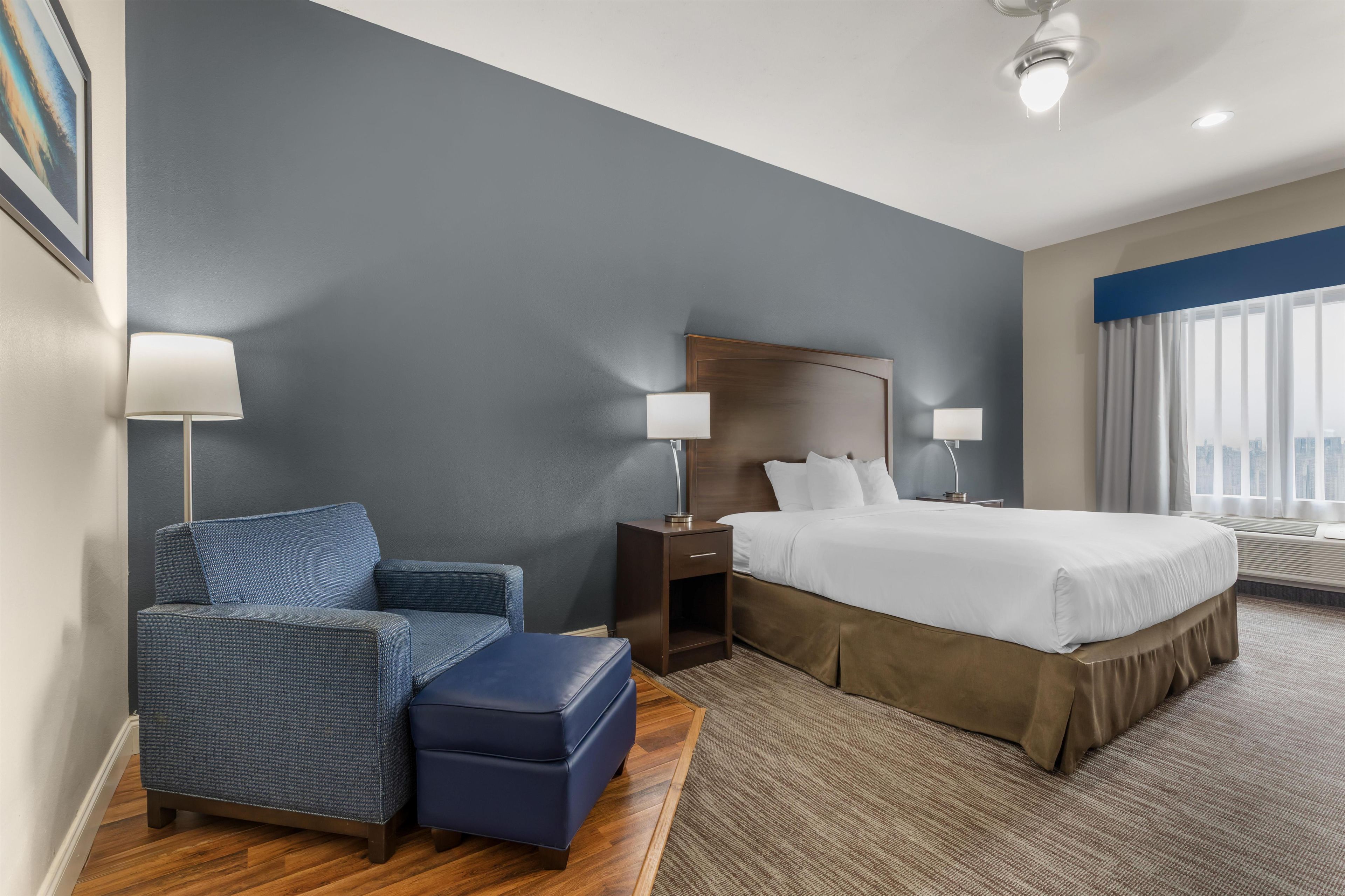 A hotel room with a bed, a chair, a nightstand, and a lamp.