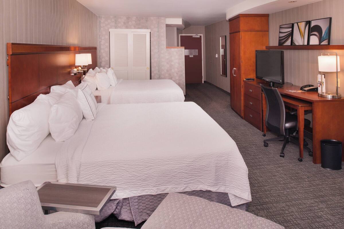 A hotel room with two beds, a desk with a computer, a chair, and a TV.