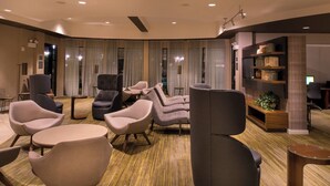 Un espace de détente moderne offrant de nombreuses options d’assises, notamment des canapés et des fauteuils, un plancher en bois et une bibliothèque agrémentée d’objets décoratifs.