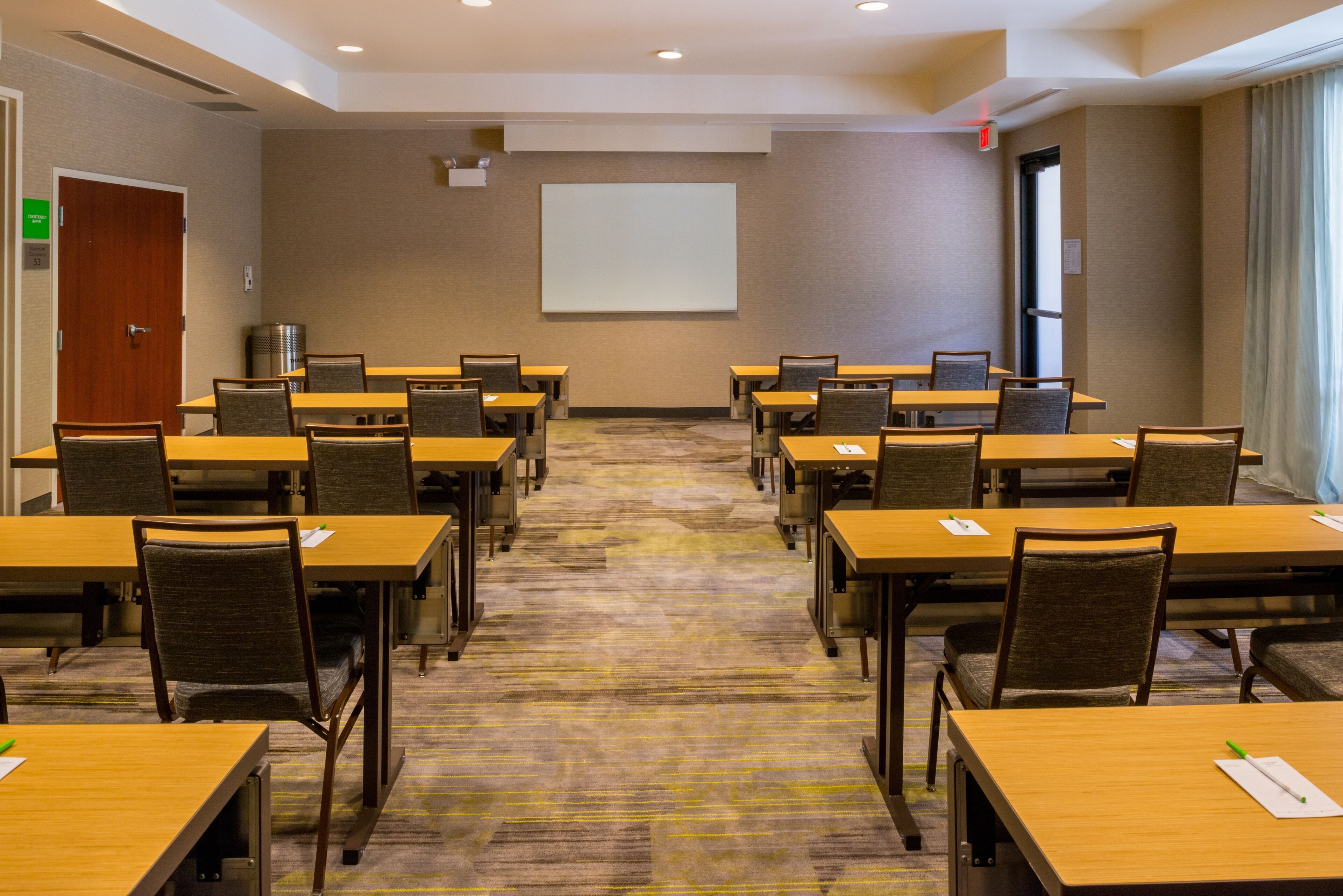 A conference room with multiple tables and chairs, a projector screen, and a carpeted floor.