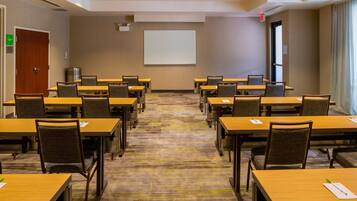 A conference room with multiple tables and chairs, a projector screen, and a carpeted floor.