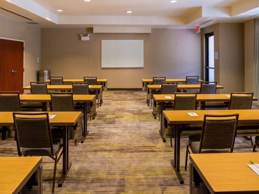 A conference room with multiple tables and chairs, a projector screen, and a carpeted floor.