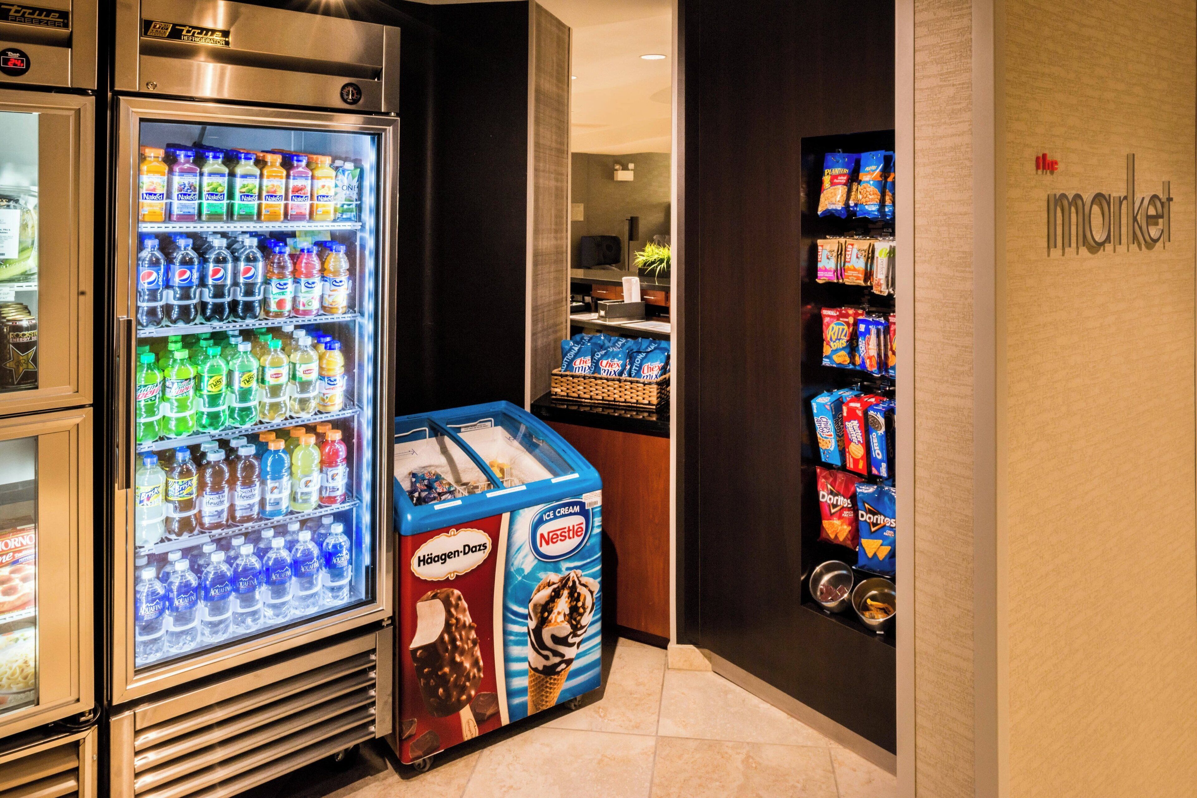 Un espace de vente proposant une variété de boissons et d’en-cas, notamment un congélateur de glaces Nestlé et un panneau indiquant les prix.