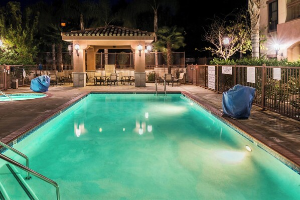 A nighttime pool area with a covered seating area, lounge chairs, and a pool with a tiled edge. - Courtyard Thousand Oaks Ventura County (Thousand Oaks)