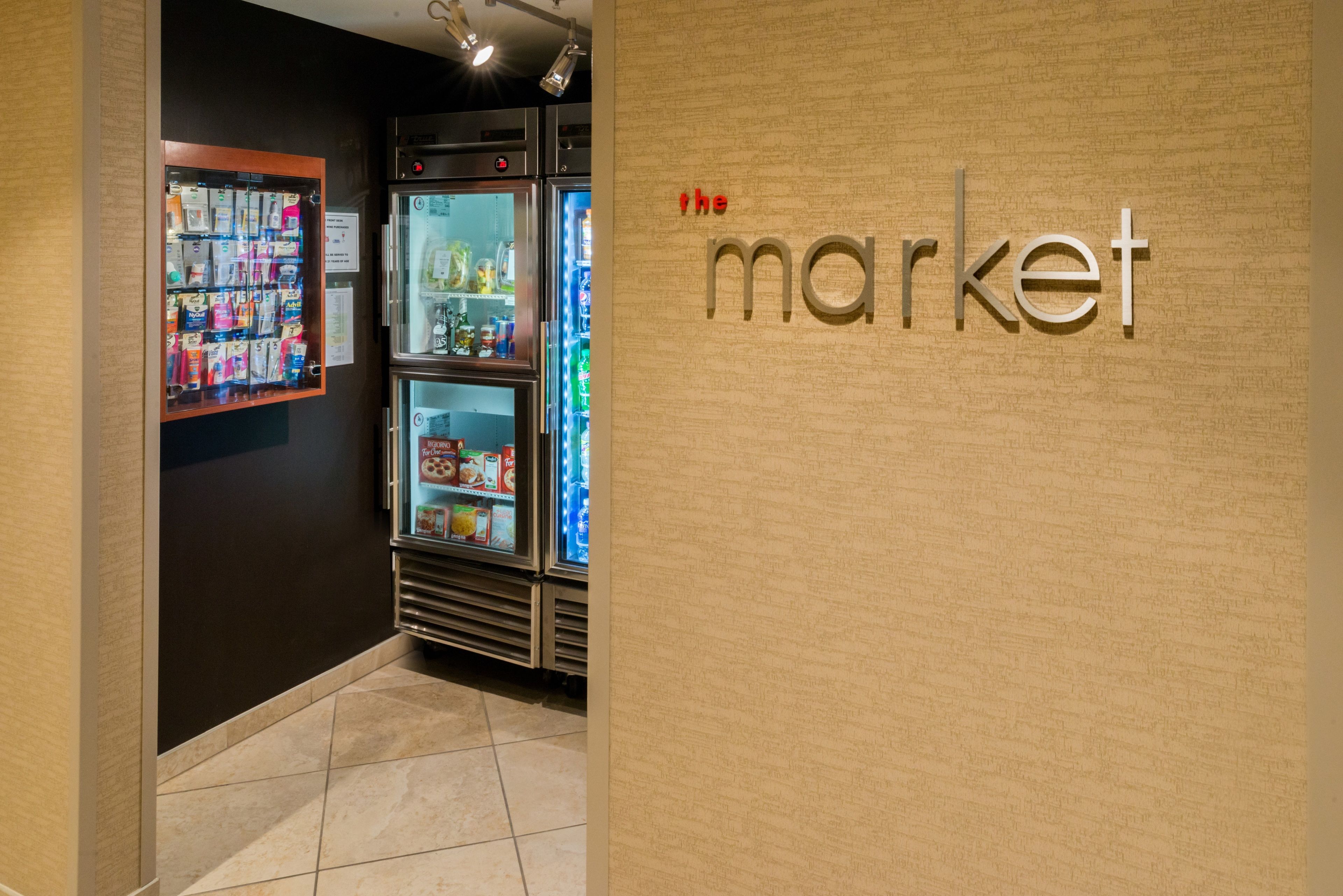 A vending machine and a refrigerator in a hallway with a wall displaying 'the market' sign.
