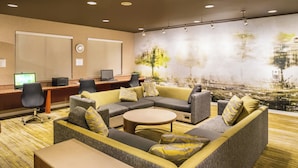 Un hall d’hôtel moderne, doté d’un grand canapé d’angle, d’une table basse ronde et d’un bureau avec des ordinateurs.