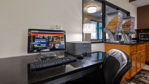 Camera d'albergo con scrivania, computer, stampante e un'ampia finestra con vista sulla città.