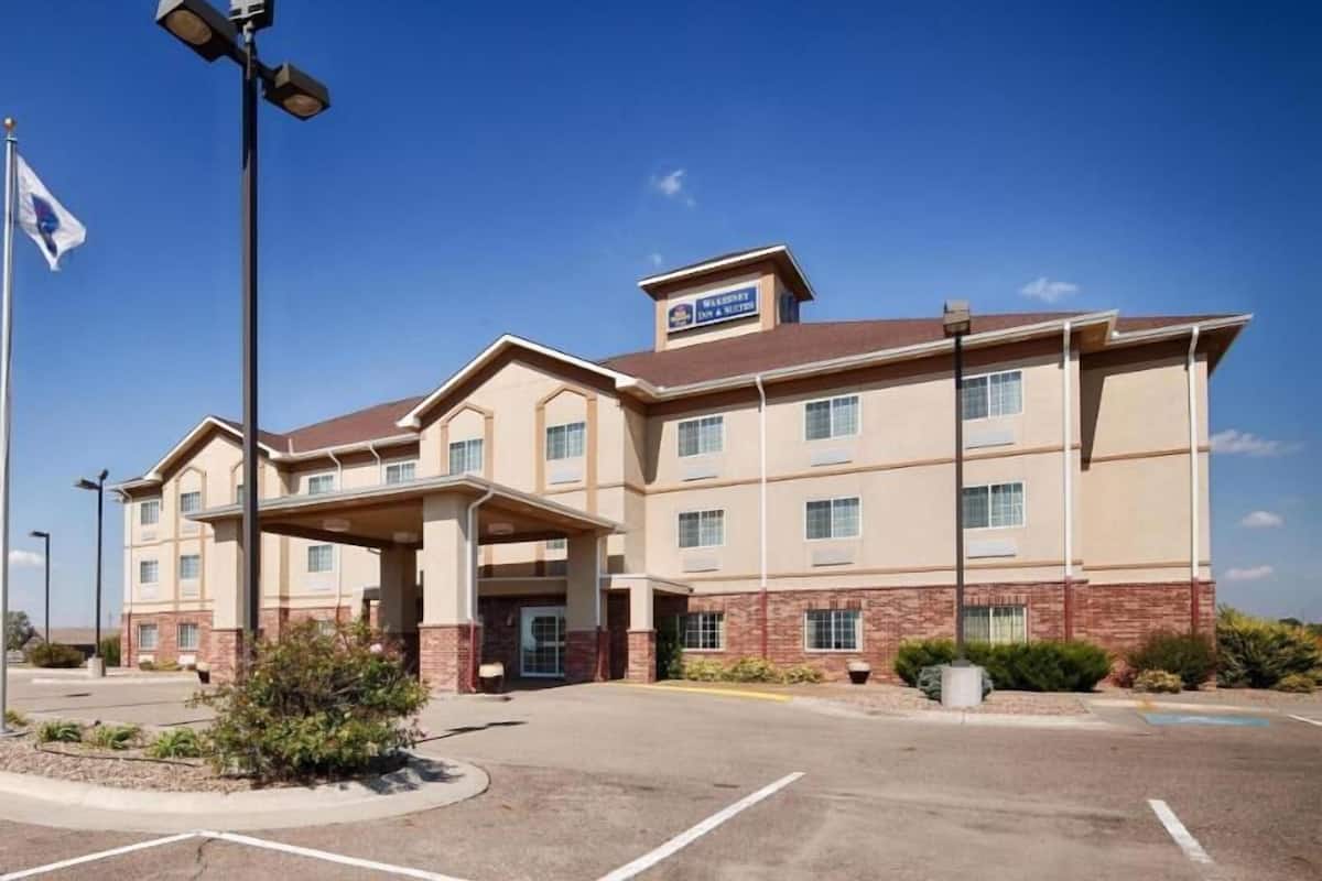 Un hotel de varios pisos con techo plano, entrada cubierta y asta de banderas.