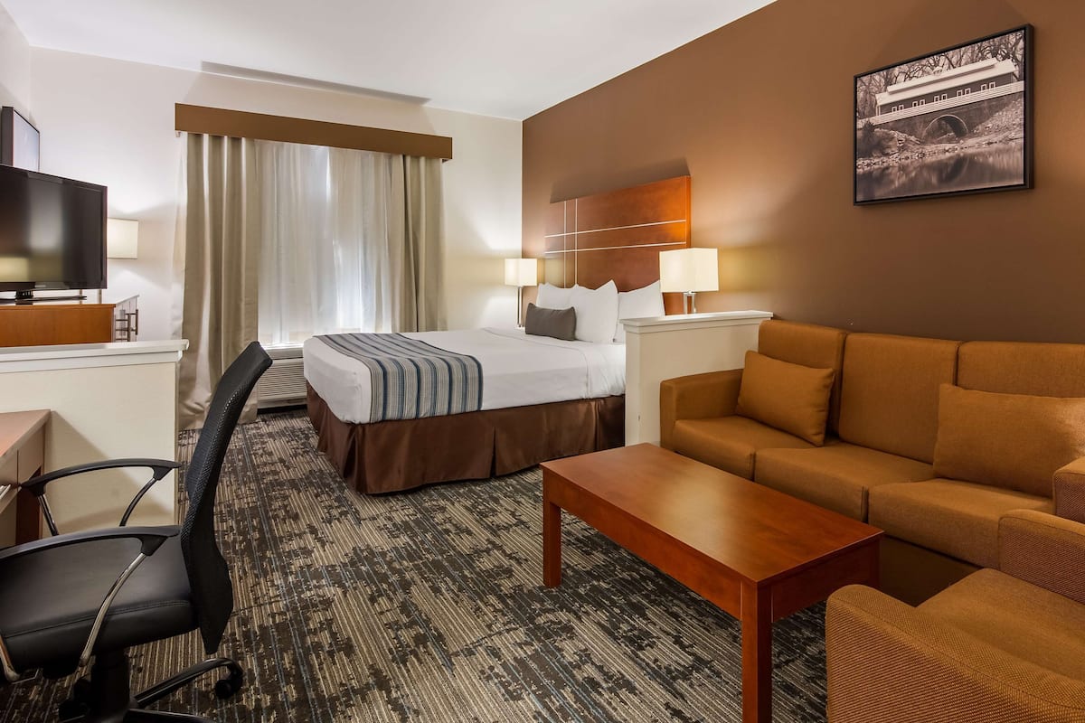 Habitación de hotel con cama, sofá, escritorio con computadora, televisión y un cuadro en la pared.