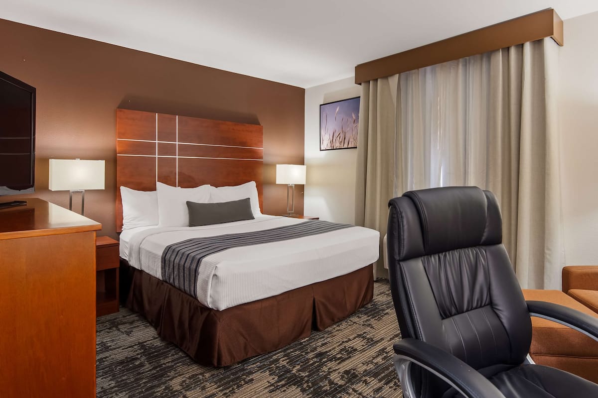 Una habitación de hotel con una cama grande, dos mesitas de noche con lámparas, un sillón de cuero y un escritorio de madera.