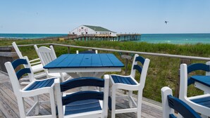 A deck with a table and chairs, overlooking a pier and the ocean. - Hilton Garden Inn Outer Banks/Kitty Hawk (Kitty Hawk)