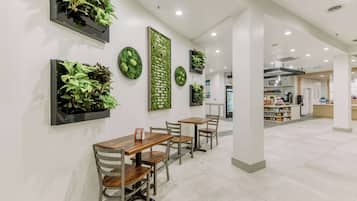 A modern interior with a dining area featuring wooden tables and chairs, surrounded by walls adorned with green plants and decorative wall art.