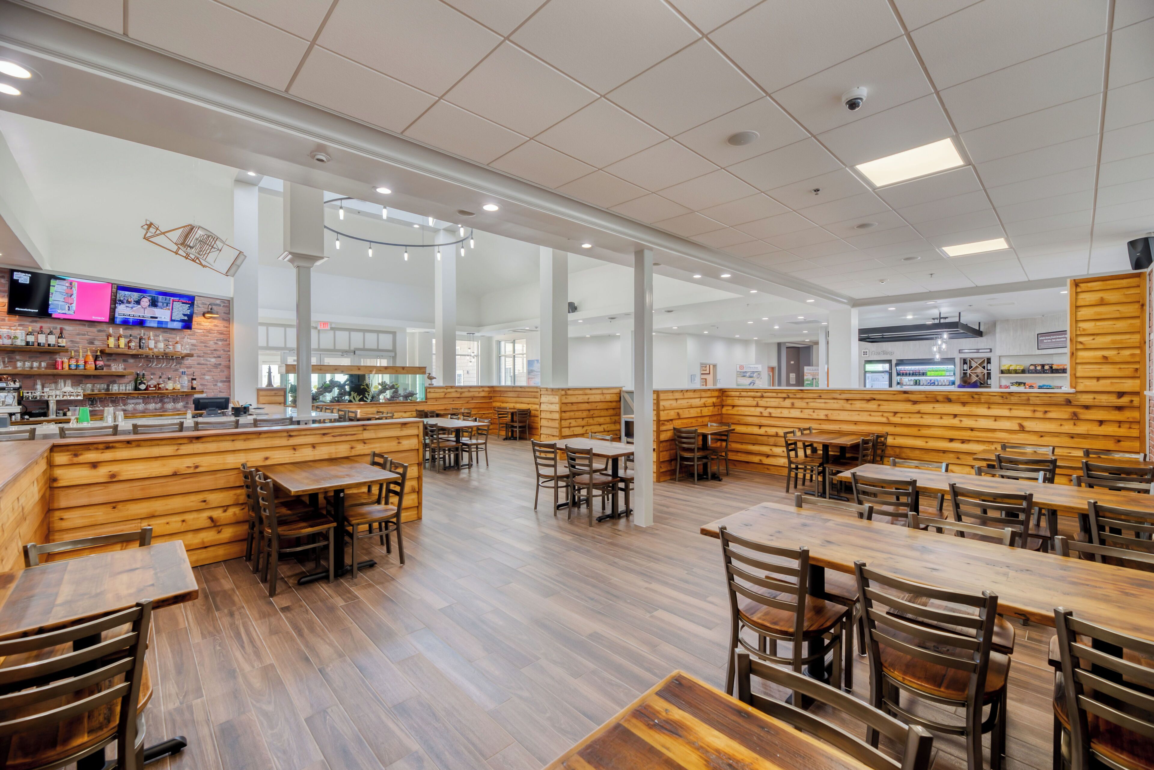 A spacious restaurant with wooden booths and tables, a bar area, and a modern ceiling design.