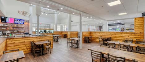 A spacious restaurant with wooden booths and tables, a bar area, and a modern ceiling design.