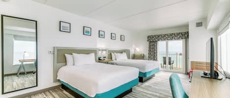 A hotel room with two beds, a desk, a chair, a large mirror, and a view of the outdoors.