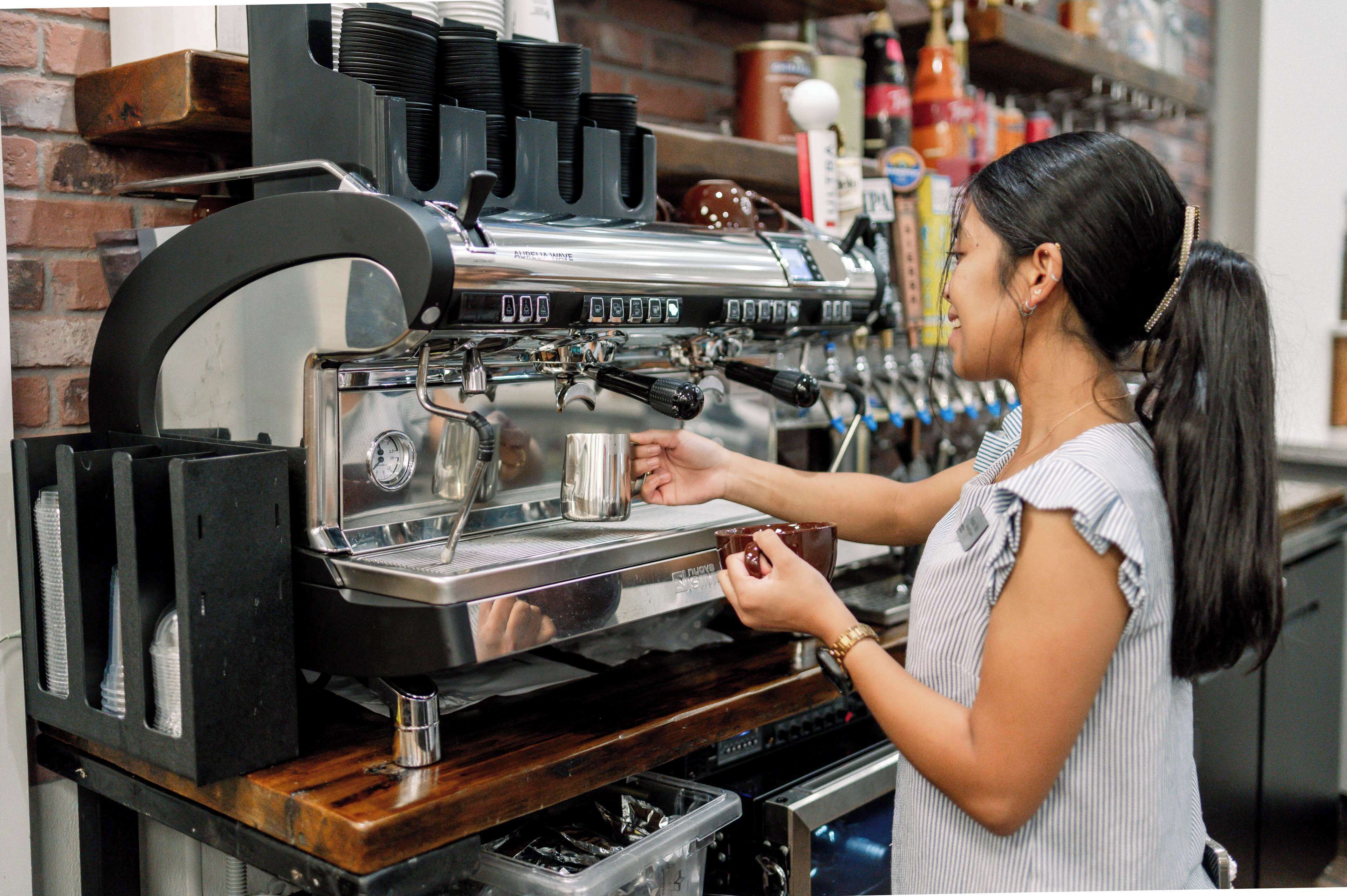 Un barista manipula una màquina d'espresso professional, amb una tassa de cafè a la mà.