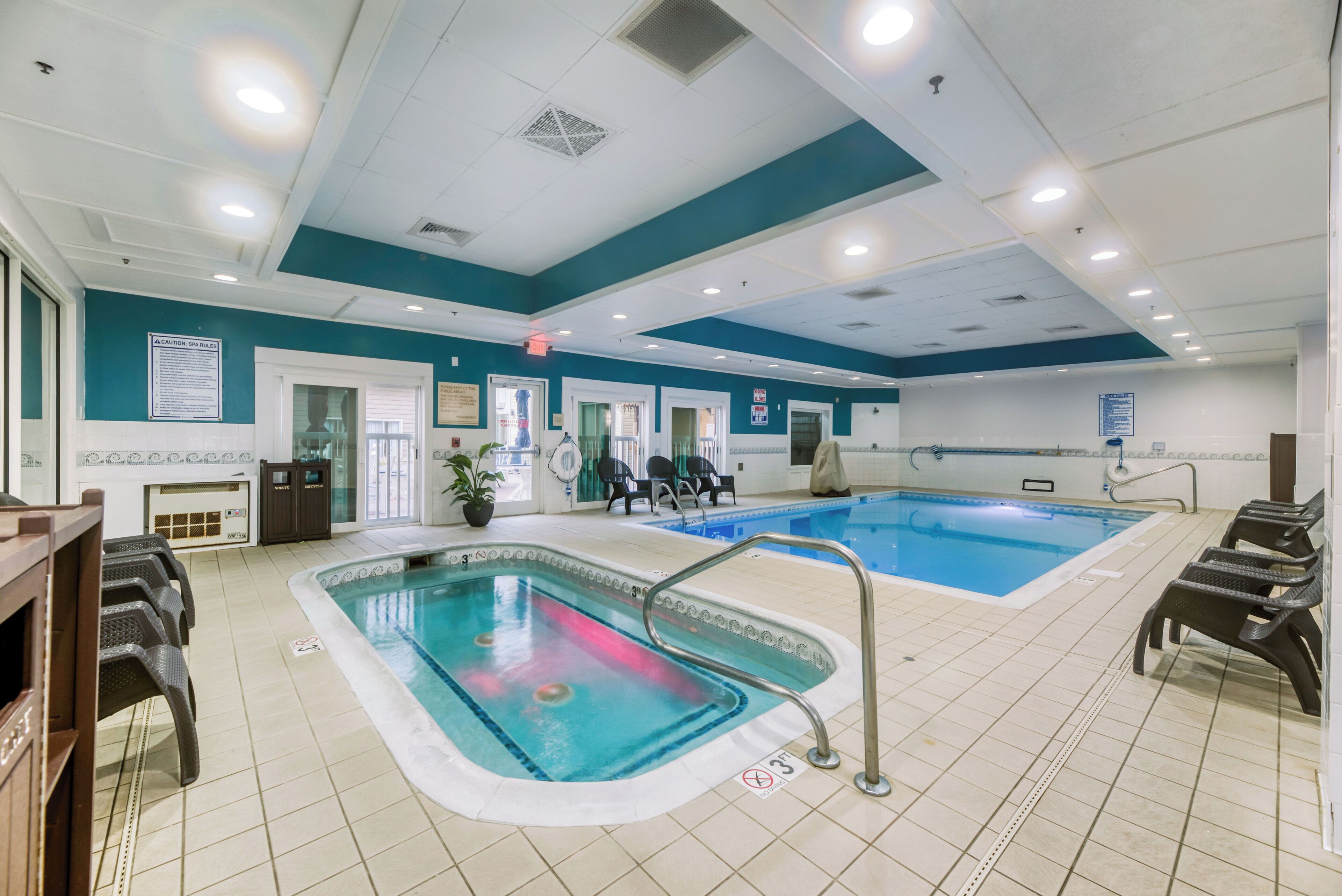 An indoor swimming pool with two lanes, surrounded by lounge chairs and a tiled floor.