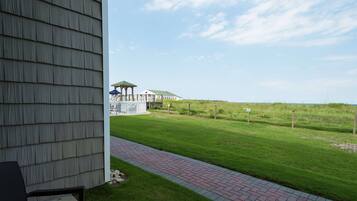A view from a porch with a brick pathway leading to a grassy area and a building with a green roof.
