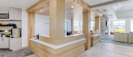 A modern reception area with a wooden reception desk, a digital display, and a seating area with red chairs.