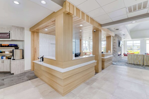A modern reception area with a wooden reception desk, a digital display, and a seating area with red chairs.