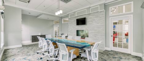 A conference room with a long table, white chairs, a mounted TV, and a stone-patterned wall.