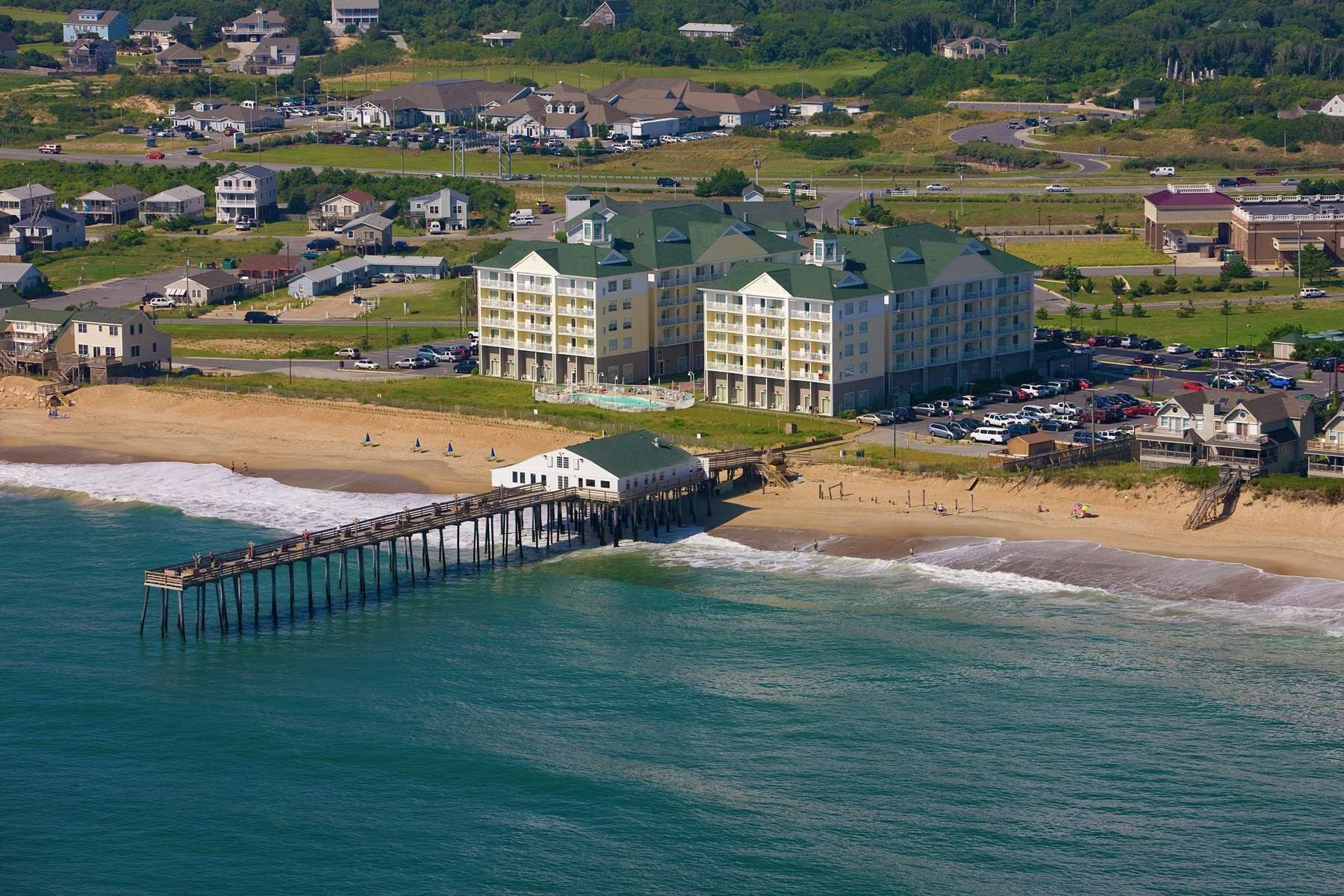 A coastal hotel with multiple buildings, a pier extending into the ocean, and a beach area.