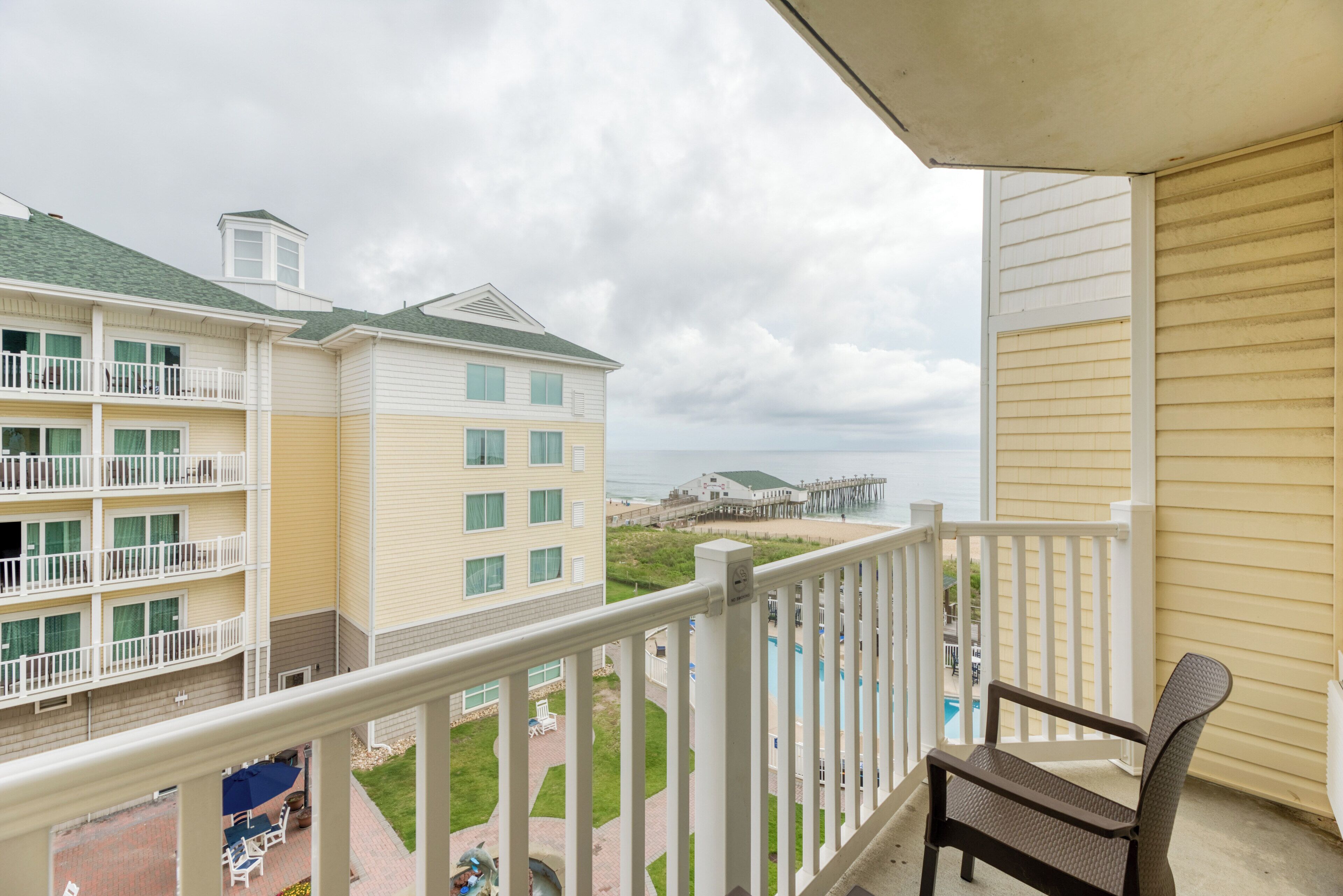 A balcony with a view of a beach and a building with multiple floors and balconies.