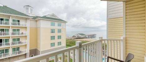 A balcony with a view of a beach and a building with multiple floors and balconies.