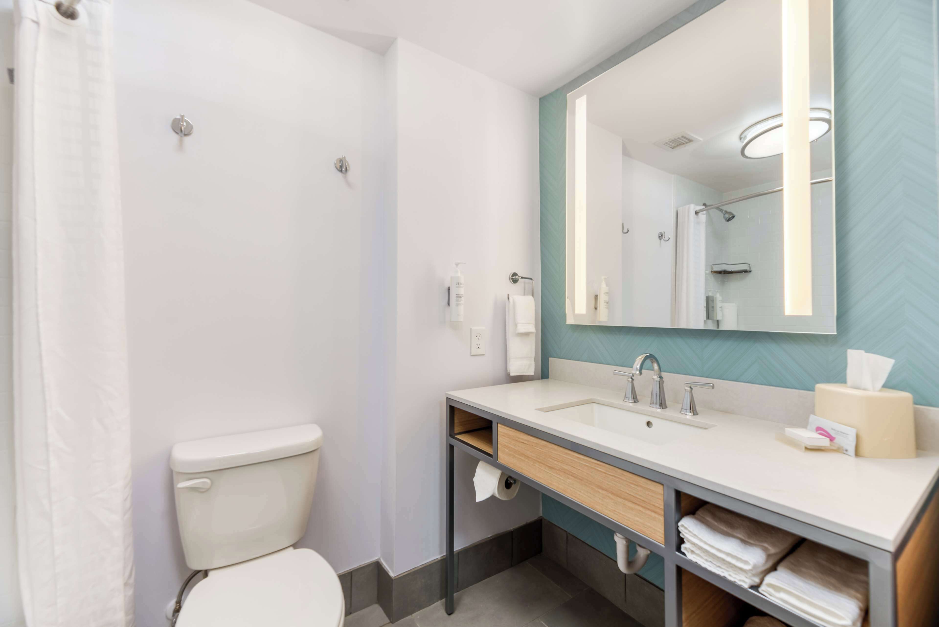 A modern bathroom with a toilet, sink, mirror, and towel storage.