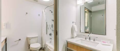 Une salle de bain moderne équipée de toilettes, d’une baignoire et d’un grand miroir au-dessus du lavabo.