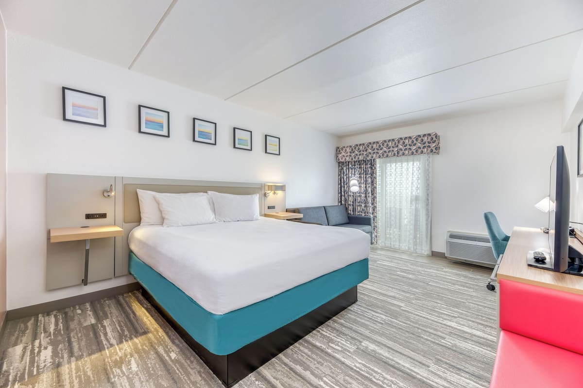 Quarto de hotel com uma cama grande, uma escrivaninha com cadeira, televisão e janela com cortinas.