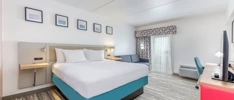 A hotel room with a large bed, a desk with a chair, a TV, and a window with curtains.