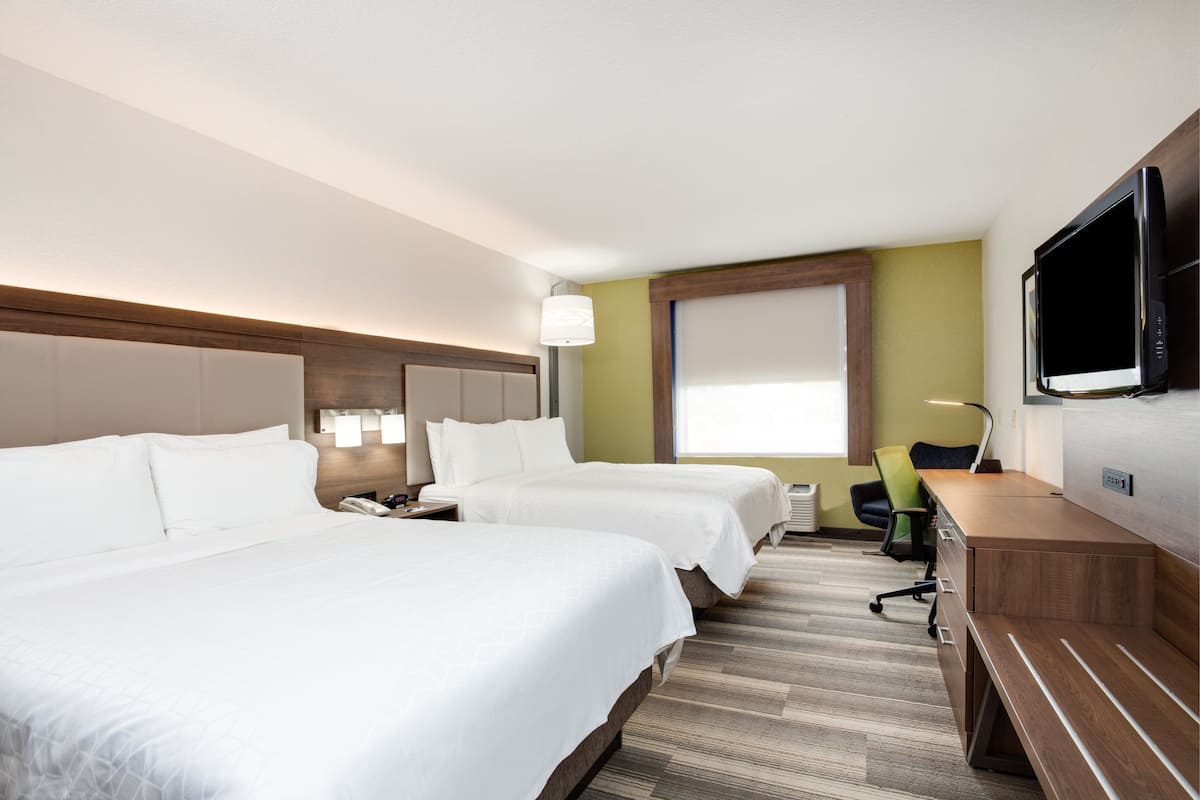 Una habitación de hotel con dos camas, un escritorio, una silla, un televisor y una ventana.