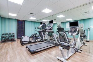 Un gimnasio con cintas de correr, elípticas y una barra de mancuernas.