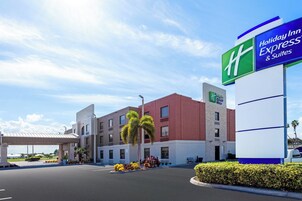 Un Holiday Inn Express & Suites con cielo despejado, zona de estacionamiento techada y jardines bien cuidados.