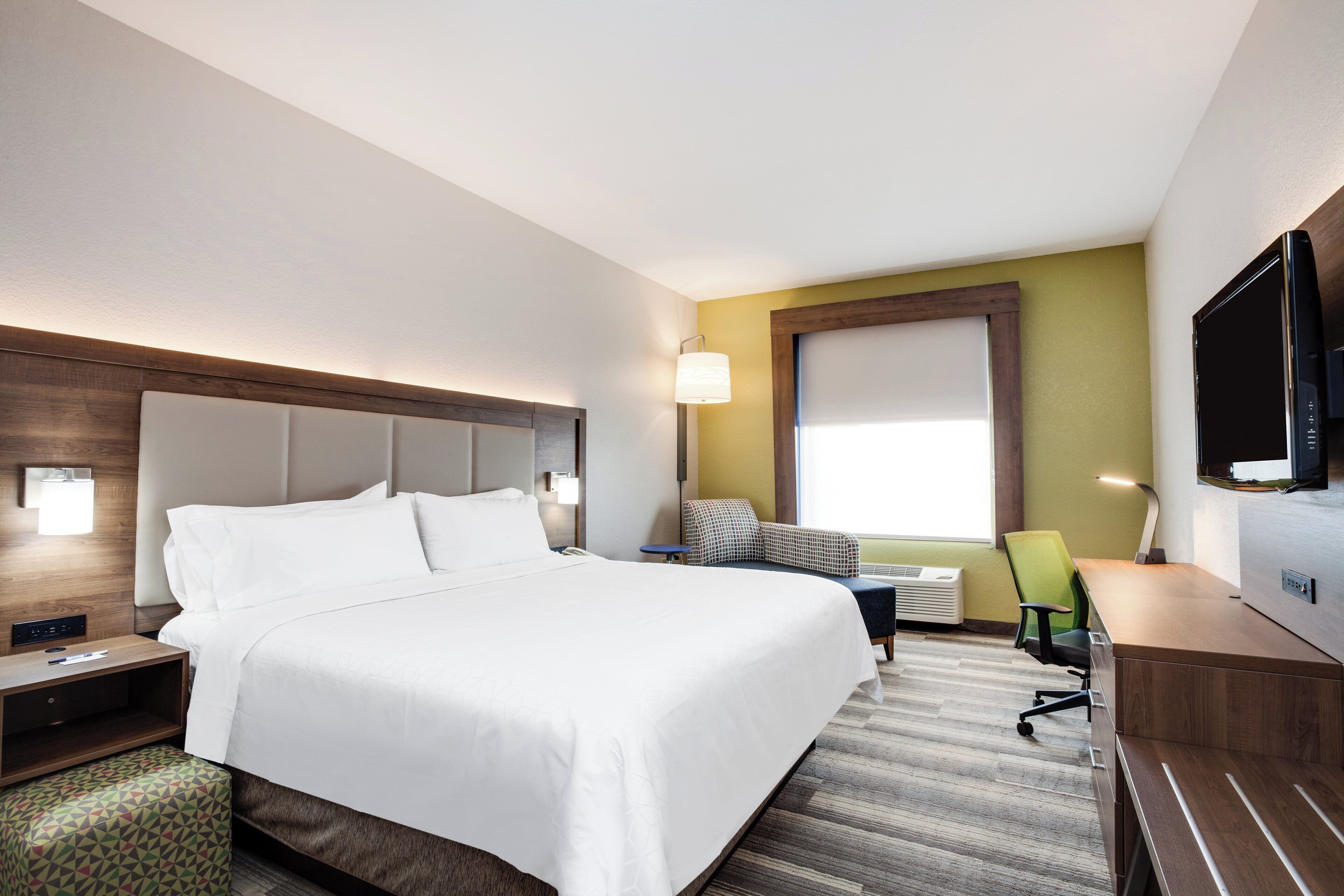 A hotel room with a large bed, a desk, a chair, a television, and a window.