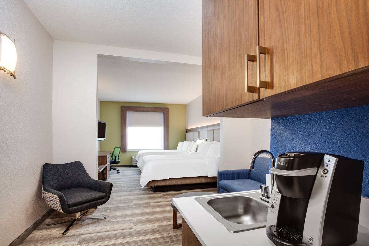 Una habitación de hotel con cama, escritorio, silla, cafetera y lavamanos.