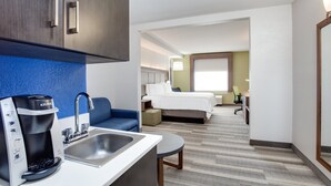 A hotel room with a kitchenette, a bed, a sofa, and a desk.