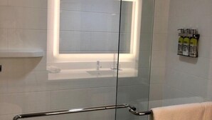 A modern bathroom with a glass shower enclosure, a visible towel rack, and a shelf with toiletries.