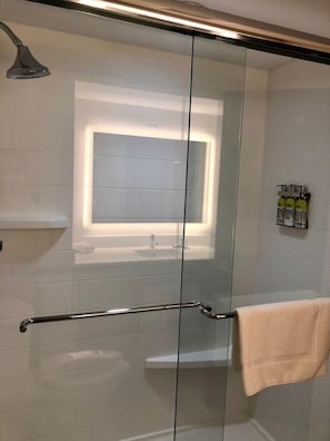 A modern bathroom with a glass shower enclosure, a visible towel rack, and a shelf with toiletries. - Holiday Inn Express Hotel & Suites Clewiston by IHG (Clewiston)