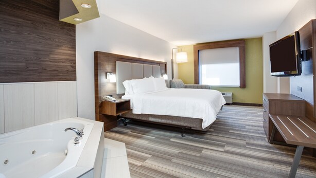 A modern hotel room with a large bed, a separate bathroom with a bathtub, a desk, and a flat-screen TV mounted on the wall.