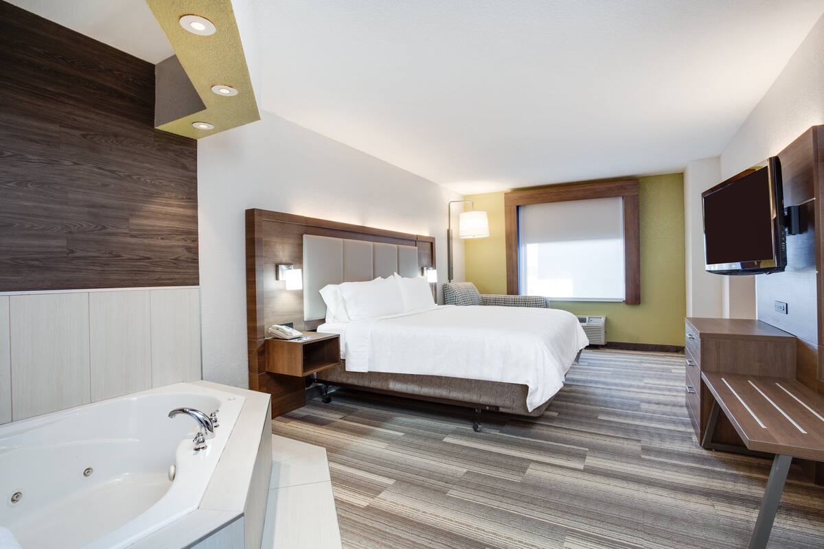 Una habitación de hotel moderna con una cama grande, un baño independiente con bañera, un escritorio y un televisor de pantalla plana montado en la pared.