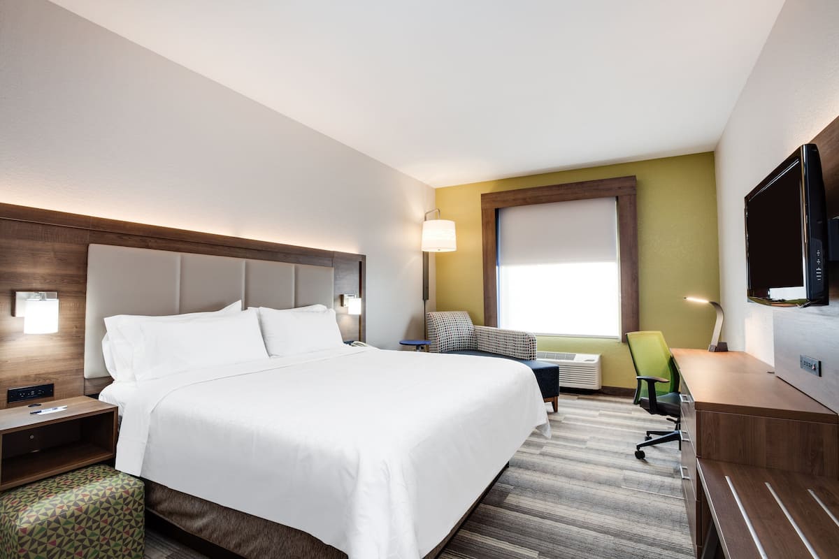 Una habitación de hotel con una cama grande, un escritorio, una silla, un televisor y una ventana con persianas.